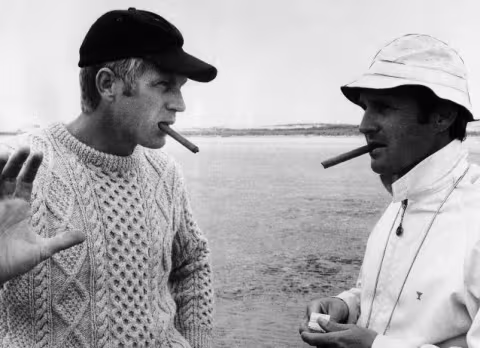 18 May 1968 --- Smoking cigars, actor Steve McQueen (left) and director Norman Jewison discuss a scene from the movie The Thomas Crown Affair. --- Image by &copy; Bettmann/CORBIS